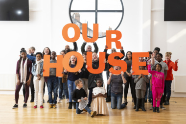 Group of adults and young people holding up letters that spell 'Our House'