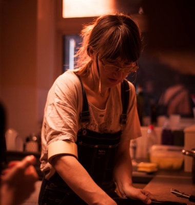 White woman with glasses and long hair tied up and glasses in dim-lit room hands in a tray.