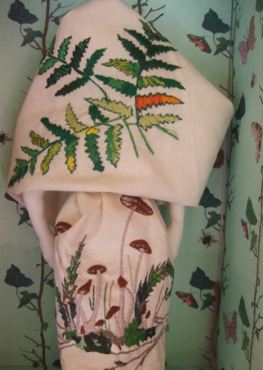 Funghi embroidery on hand-made doll with tree pattern behind.